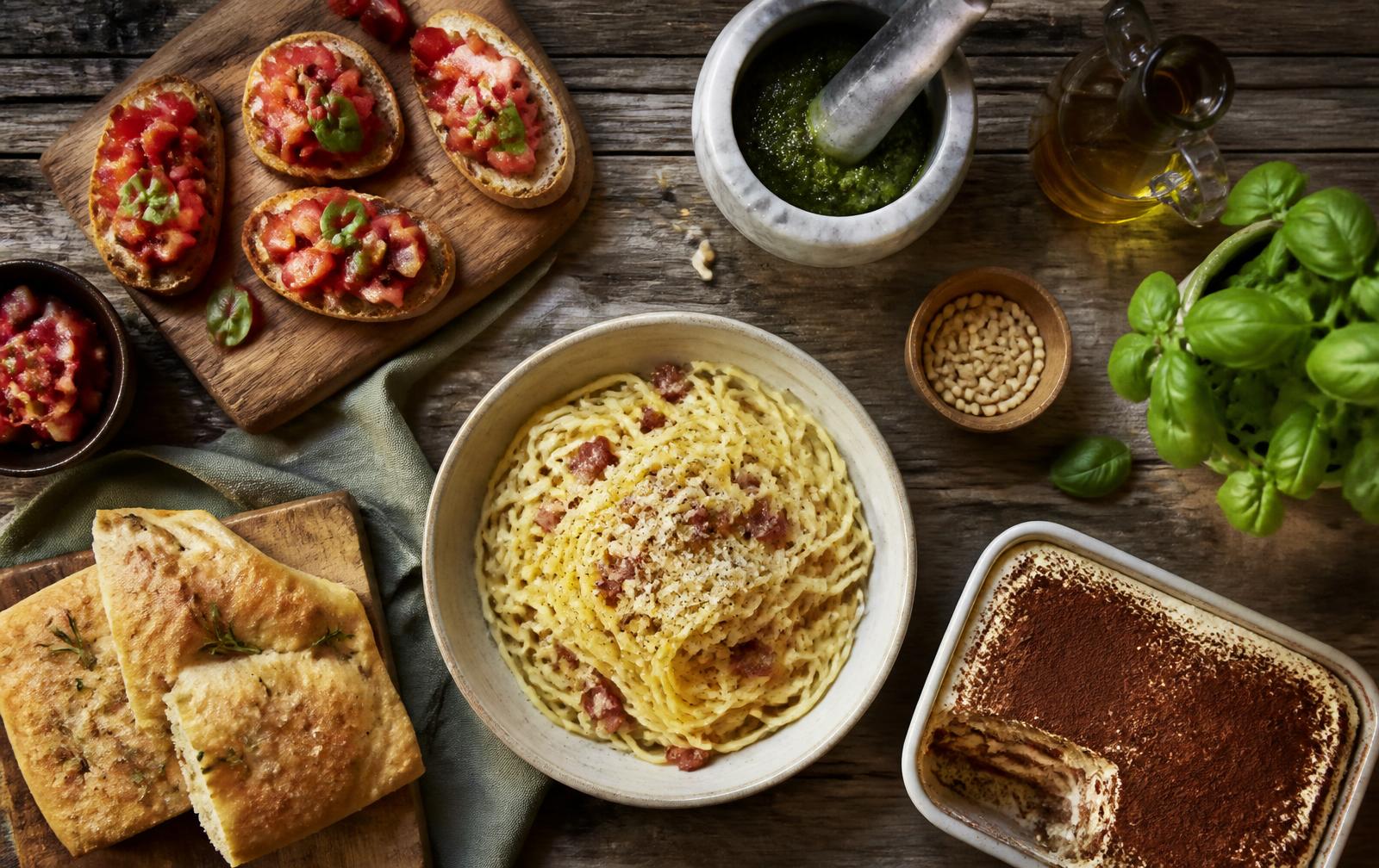 Italienska recept på ett rustikt träbord – carbonara, bruschetta, pesto, focaccia och tiramisù