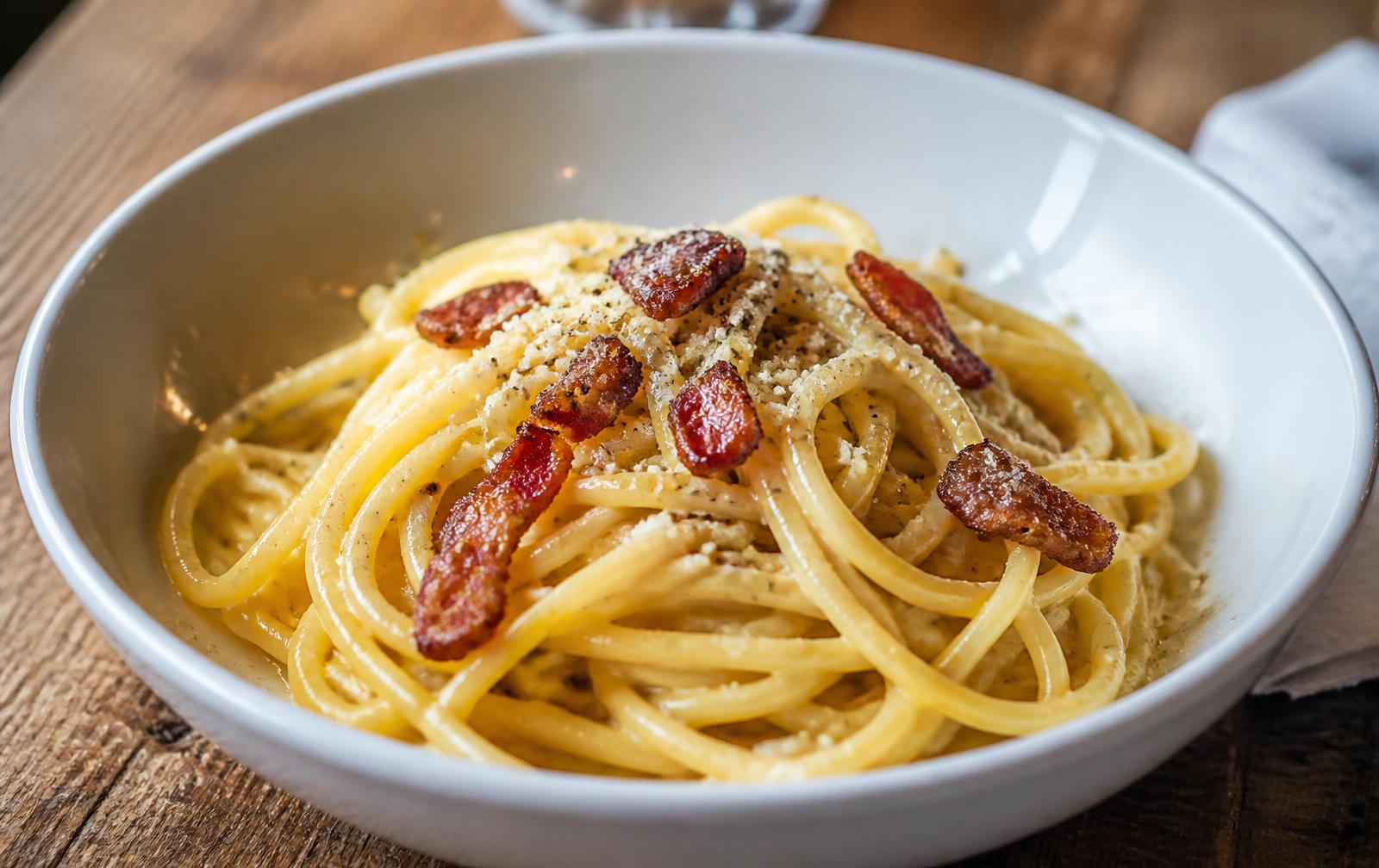 Spaghetti carbonara i vit skål med krispig guanciale, pecorino och svartpeppar